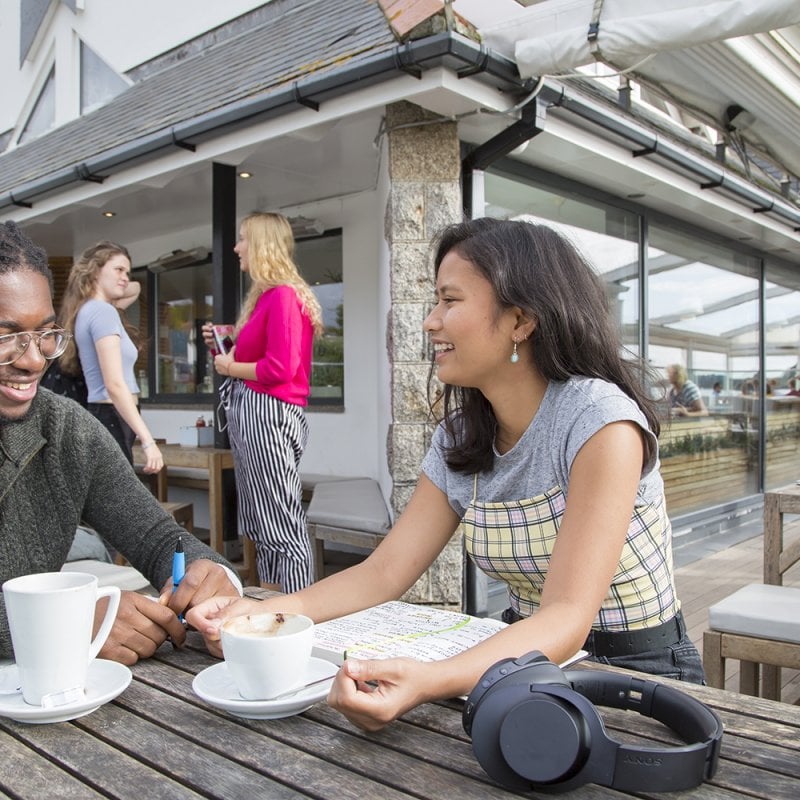 Male and female student talking at a bench with coffee cups and headphones 