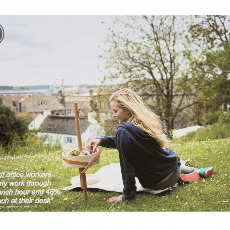 Girl sitting on grass and eating out of a tray table held by a stick in the ground.
