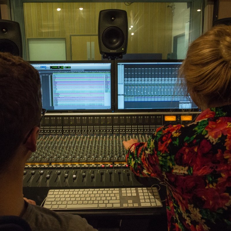 View from behind two students adjusting controls on mixing desk in studio