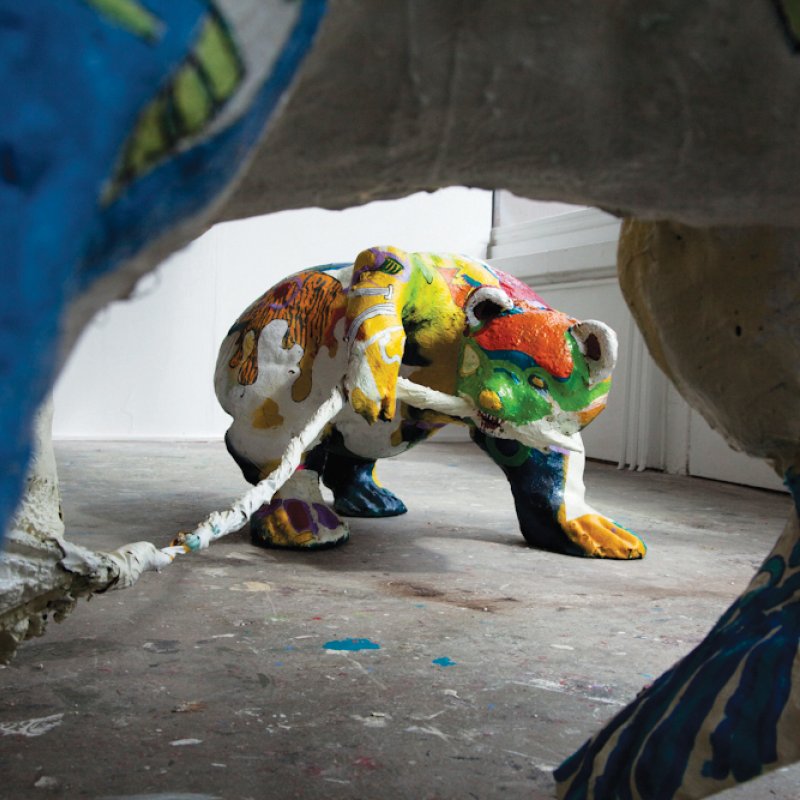 Sculpture of bear painted in bright colours with rope in mouth.