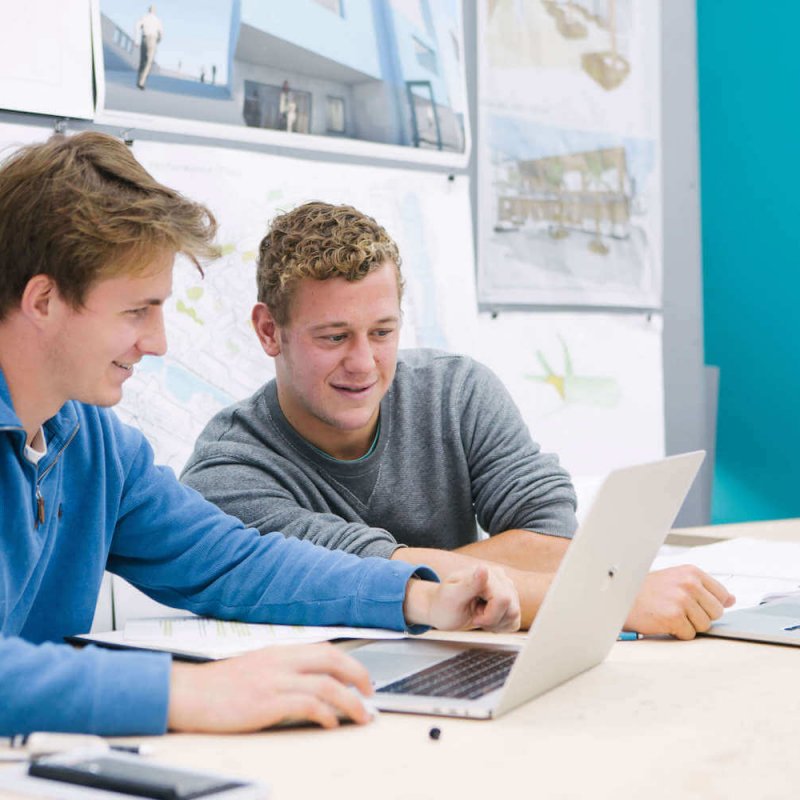 Two male students seated while looking at a laptop