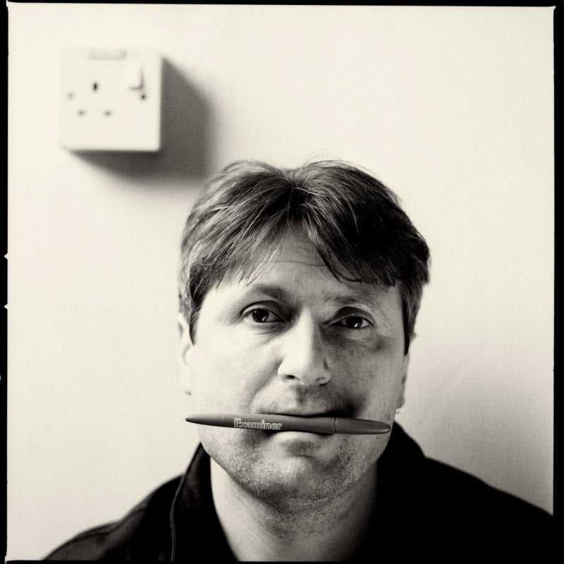 Portrait of Simon Armitage, with a pen in his mouth.