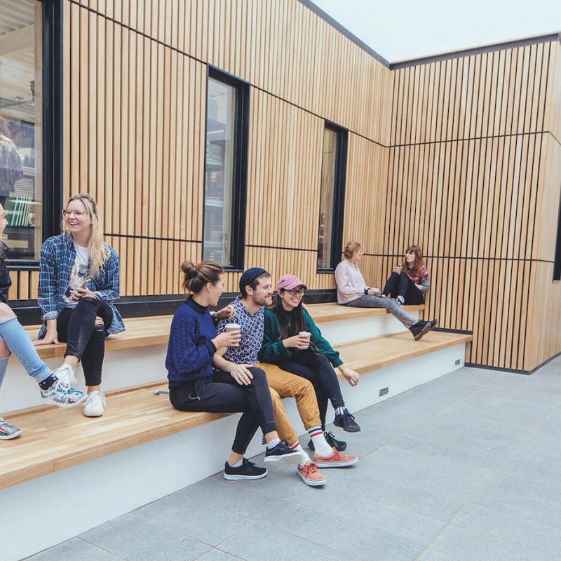 Falmouth University students sitting on steps with a wooden cladded wall behind