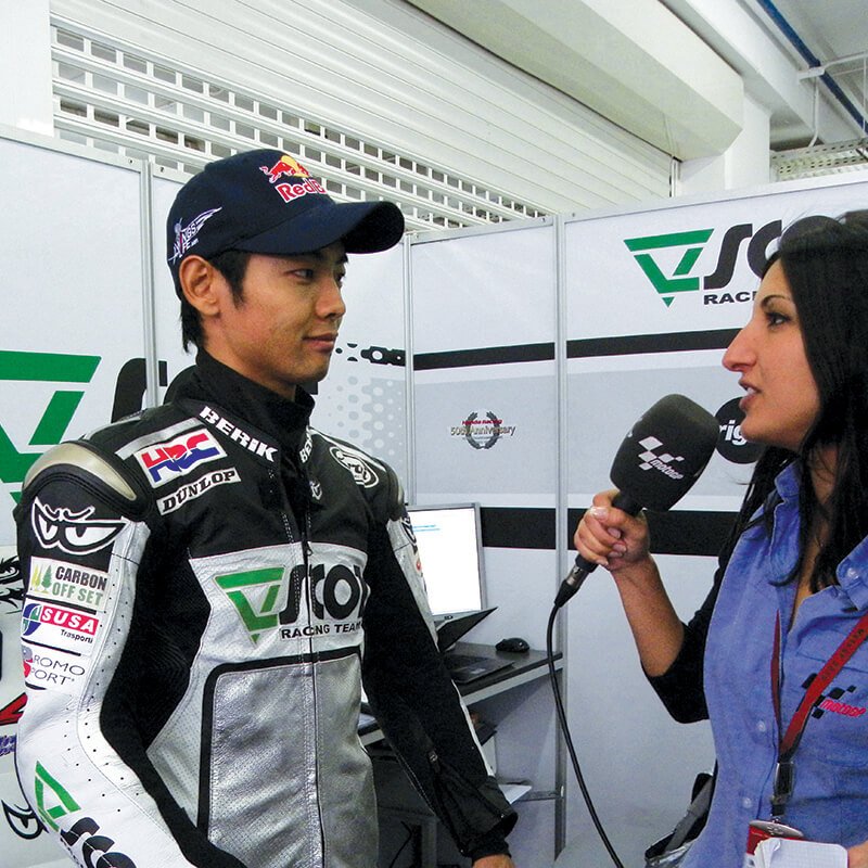 Graduate interviewing racing driver in leathers and Red Bull cap.