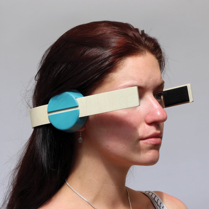 Woman wearing wooden strap around the back of head and in front of her eyes with turquoise circles by her ears.