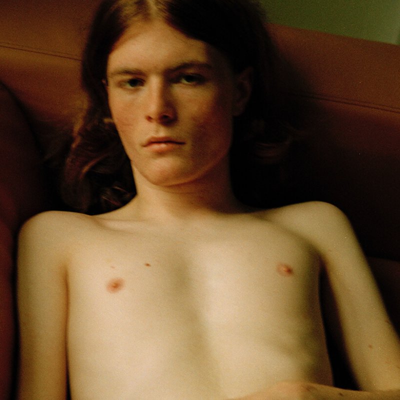 young man with long brown hair, lying down topless