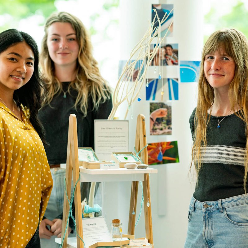 Three Business students stood in front of a stand of their work.
