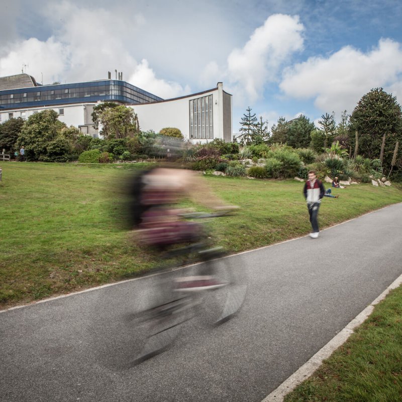A student riding a bike on a path on Penryn Campus