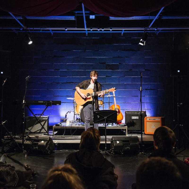 Musician playing guitar on blue lit stage at the Falmouth Live Lounge