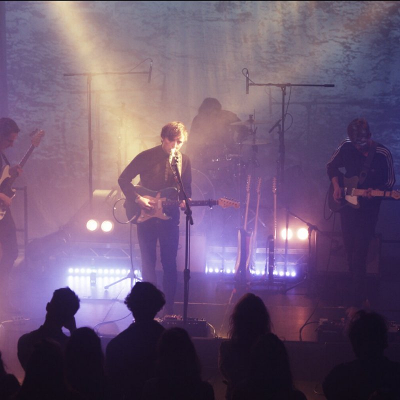 Band with guitarists and drummer on stage with blue and purple lights.