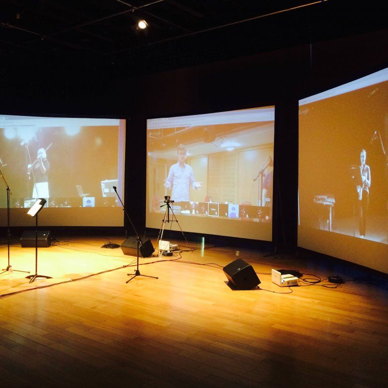 A woman playing the clarinet in front of three digital screens