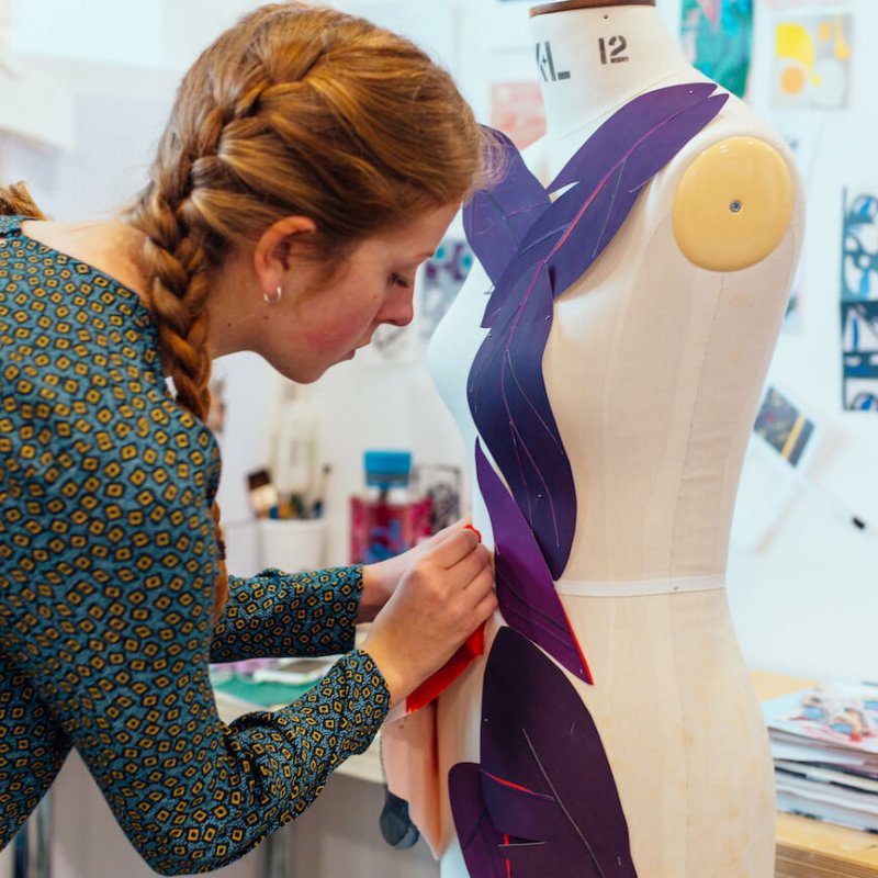 Costume Design student pinning purple fabric leaves to mannequin.