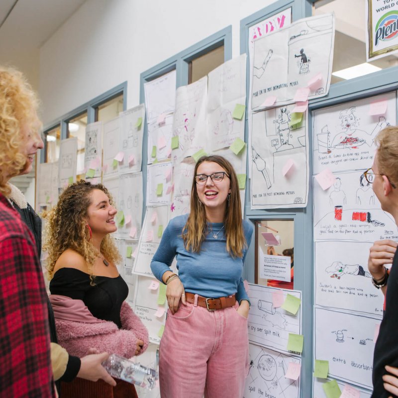 Creative advertising students discussing in front of an ideas wall.