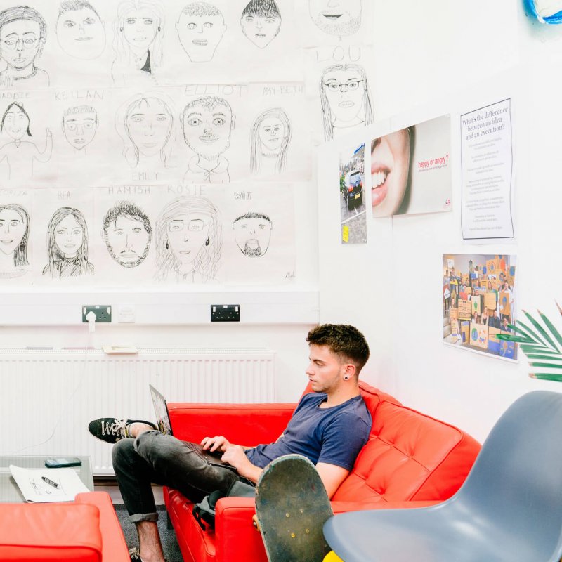 Male Creative Advertising student sitting on a red sofa at Falmouth University