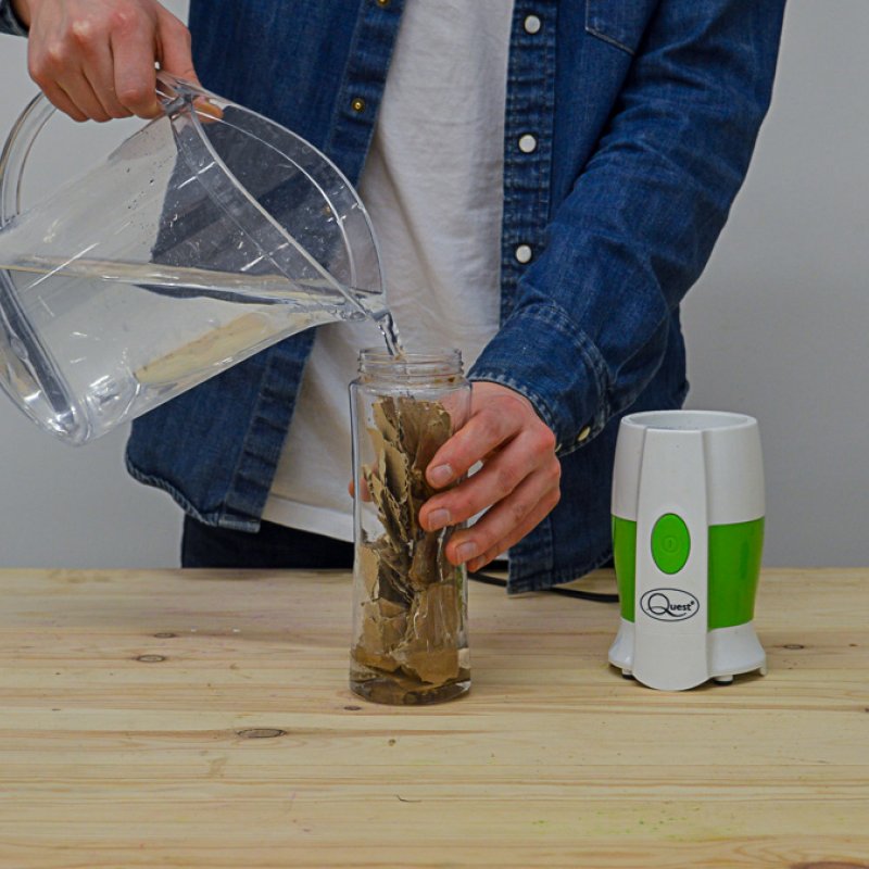 A person pouring a jug of water into a glass full of cardboard