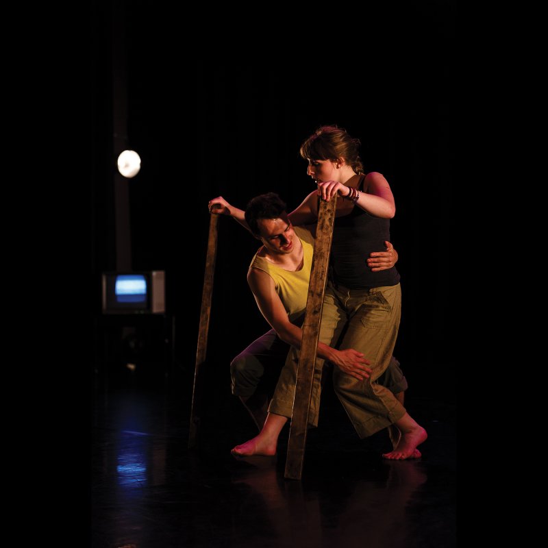 Dancers moving together on stage with planks of wood supporting hands.