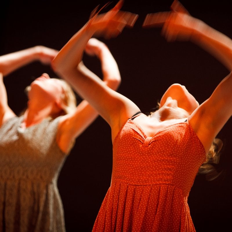 Dancers in dresses throwing hands and heads backwards.