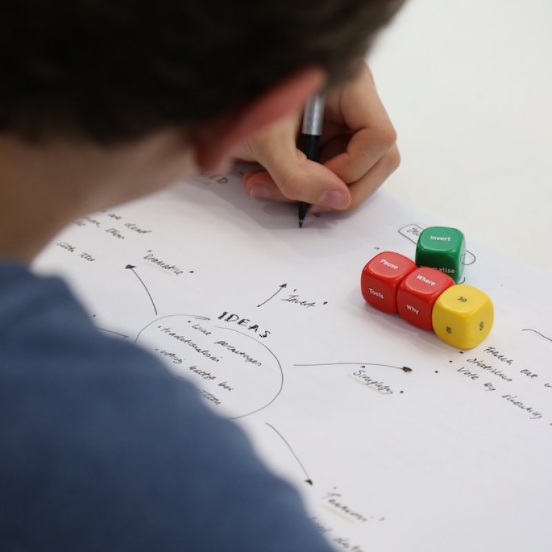 Person writing a spider diagram on a sheet of paper with dice and pen.