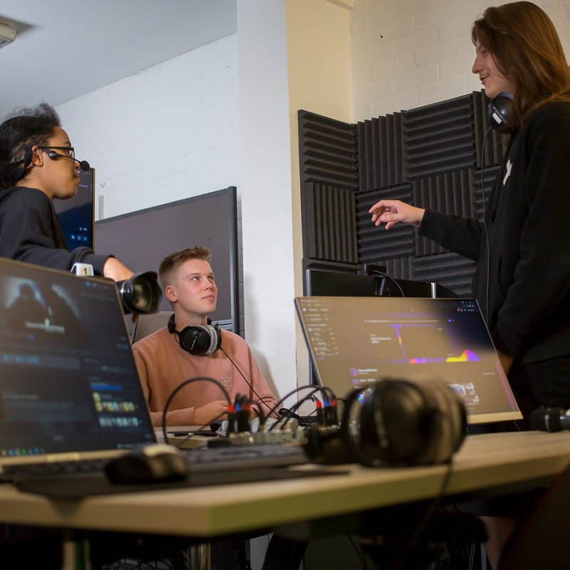 Three Esport Falmouth University students talking in a studio with screens