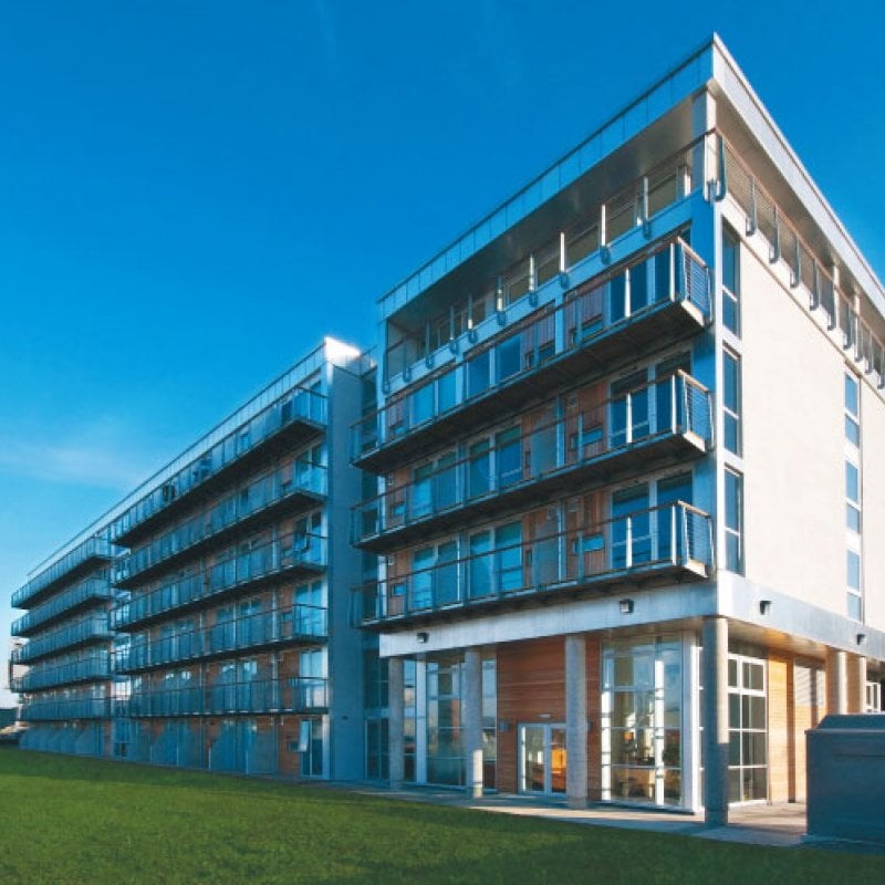 five-storey apartment building with glass balconies, grass and blue sky