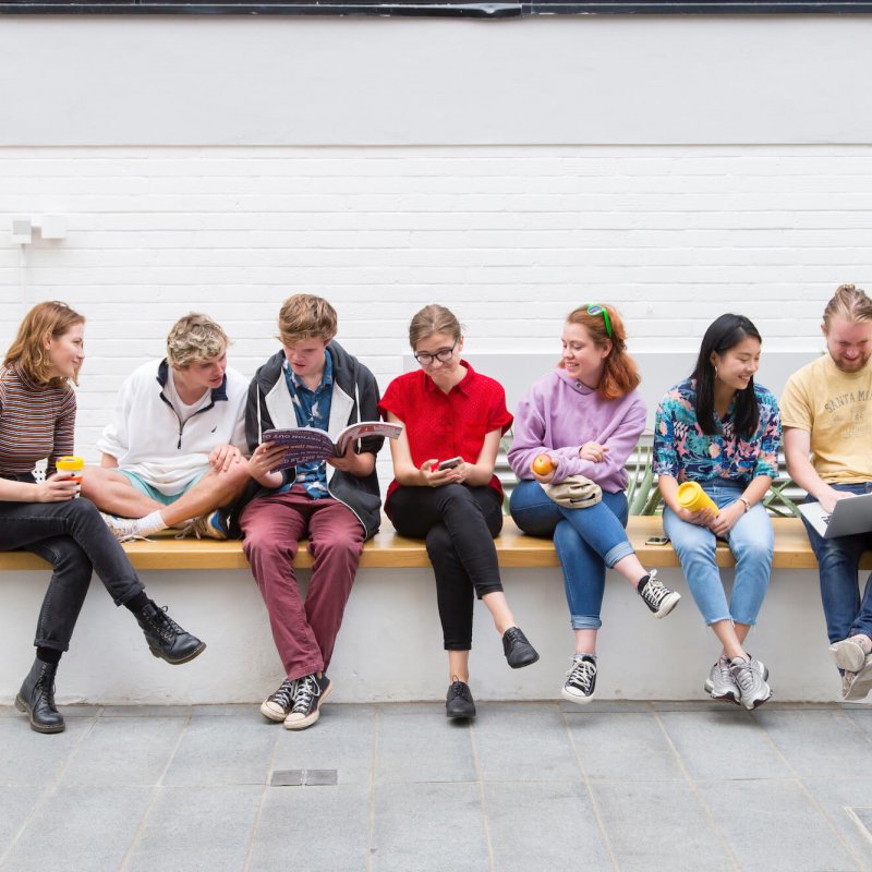 A group of Falmouth University students sitting on a wall inside a white building
