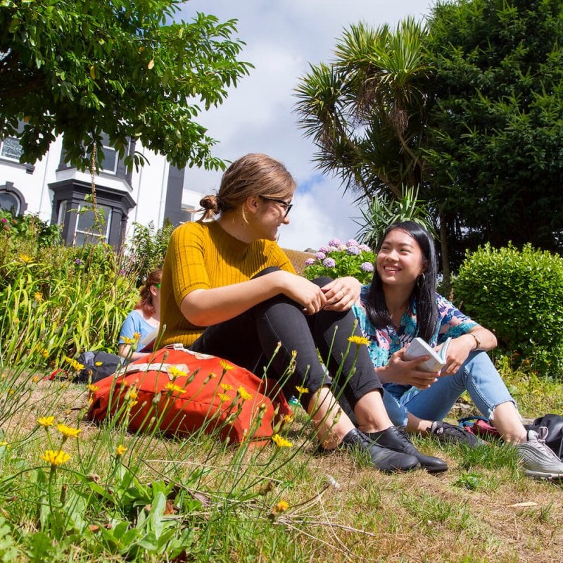 Falmouth University students sat and chatting in gardens on Falmouth Campus