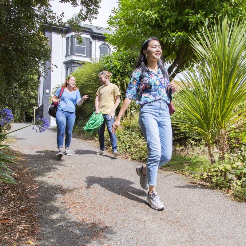 Three falmouth students walking along a path with plants