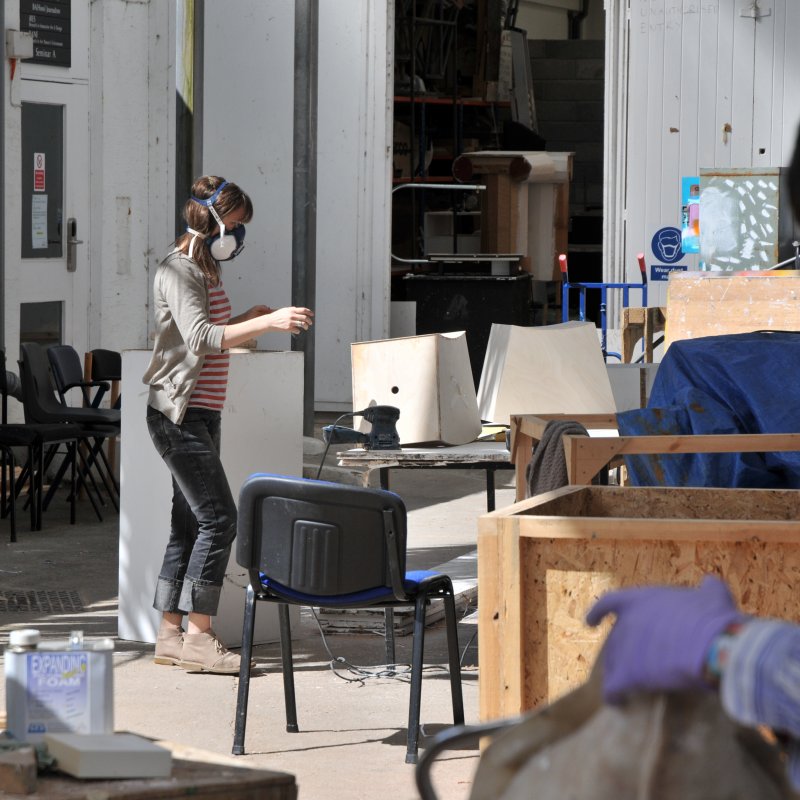 A Falmouth student with a mask on working on a 3D piece outdoors.