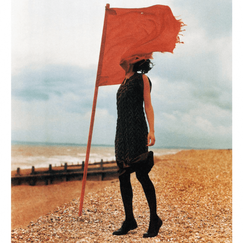 A fashion model wearing black clothes on a beach with a red flag