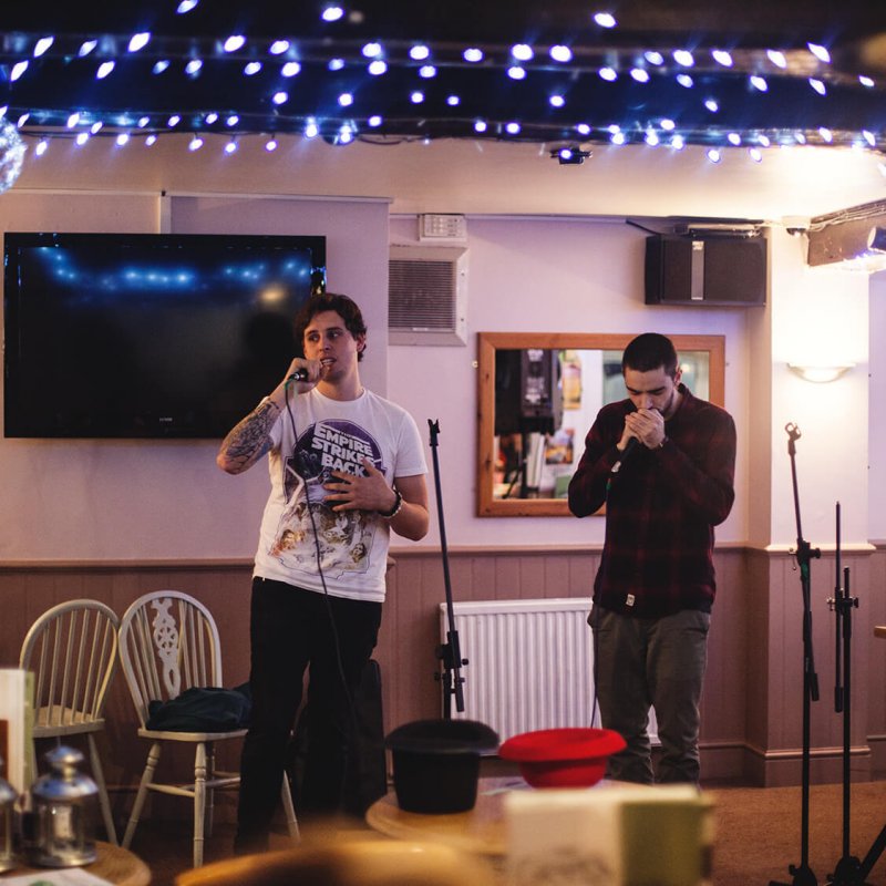 Two Creative Writing students on stage at a poetry slam with blue fairy lights on the ceiling