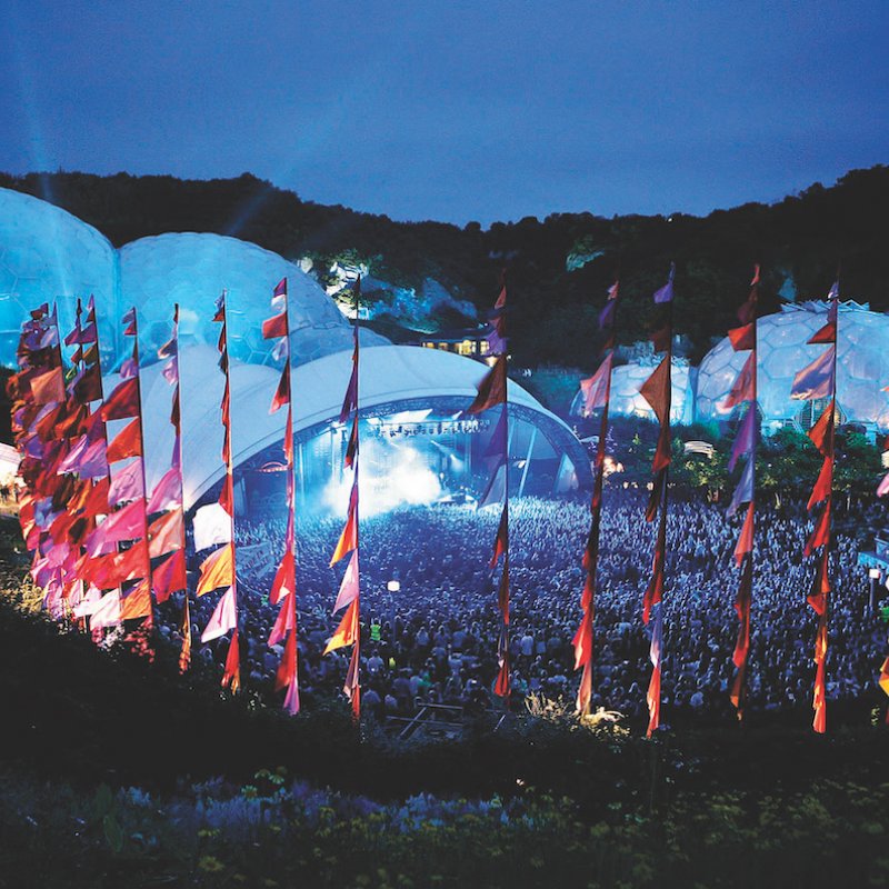 Eden Project biomes lit in blue light with red, pink and purple flags in the foreground.