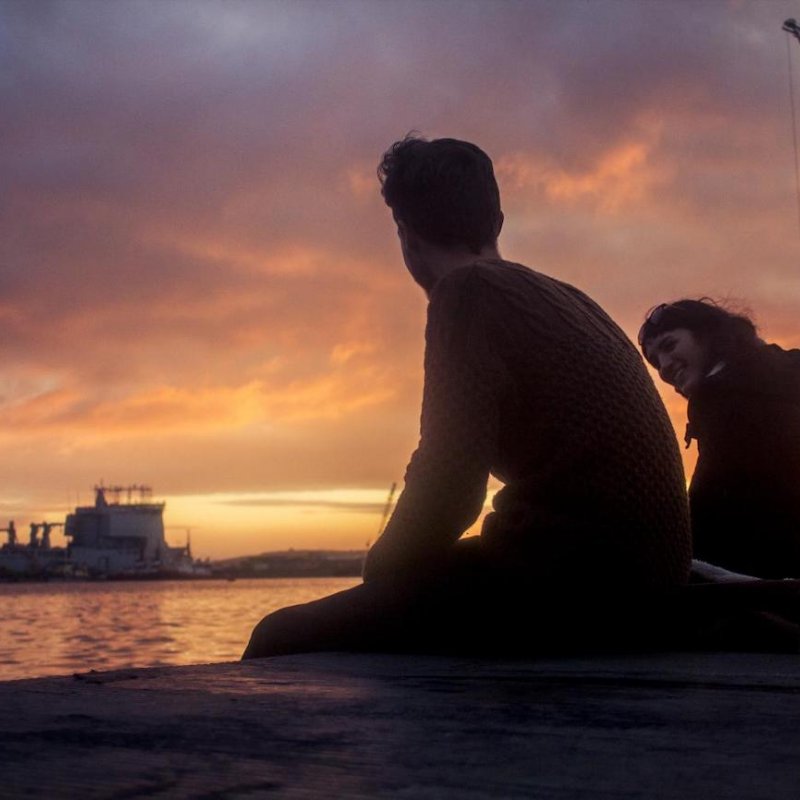 Two students sat watching the sunset with Falmouth docks in the background