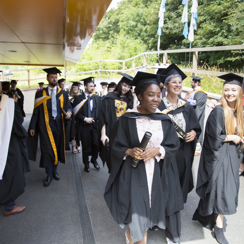 Smiling Falmouth University graduates in gowns and hats walking out of graduation ceremony 2019.
