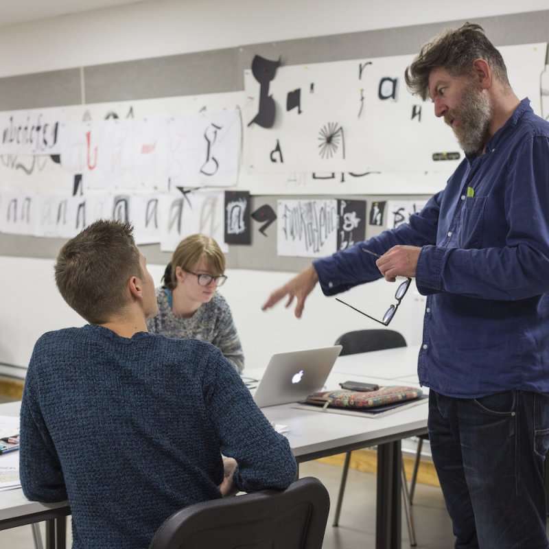 Lecturer discussing with student and gesturing with hand.