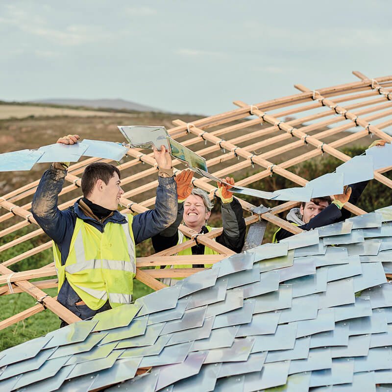 Students adding a roof to a wooden curved structure.