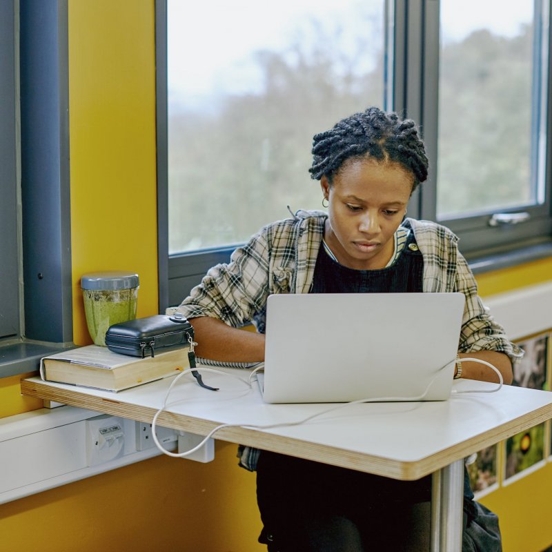 A student sat at a table with a laptop and yellow walls