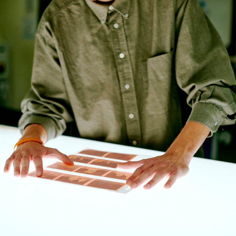 Falmouth student wearing a green shirt looking at film negatives on a light box.