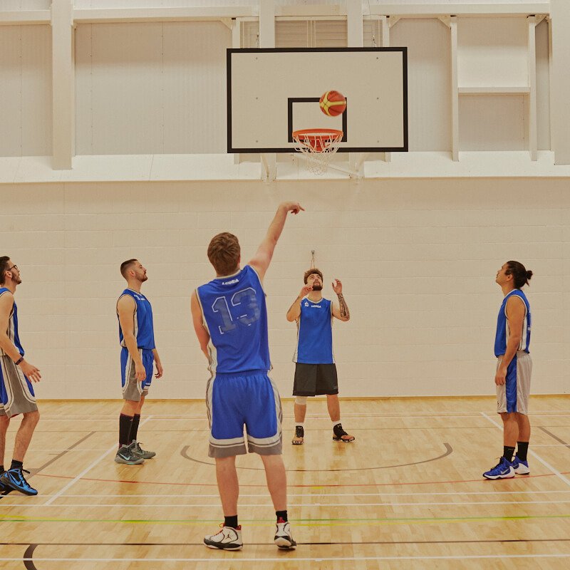 Male Falmouth students dressed in blue playing basketball inside a sports hall