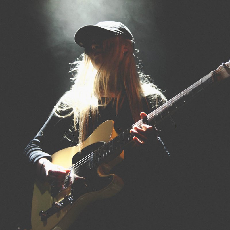 Blonde girl with cap on, playing guitar.