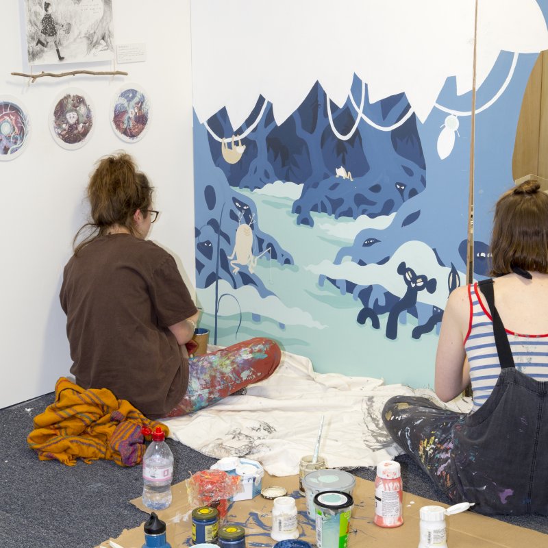 Two female students painting a large canvas