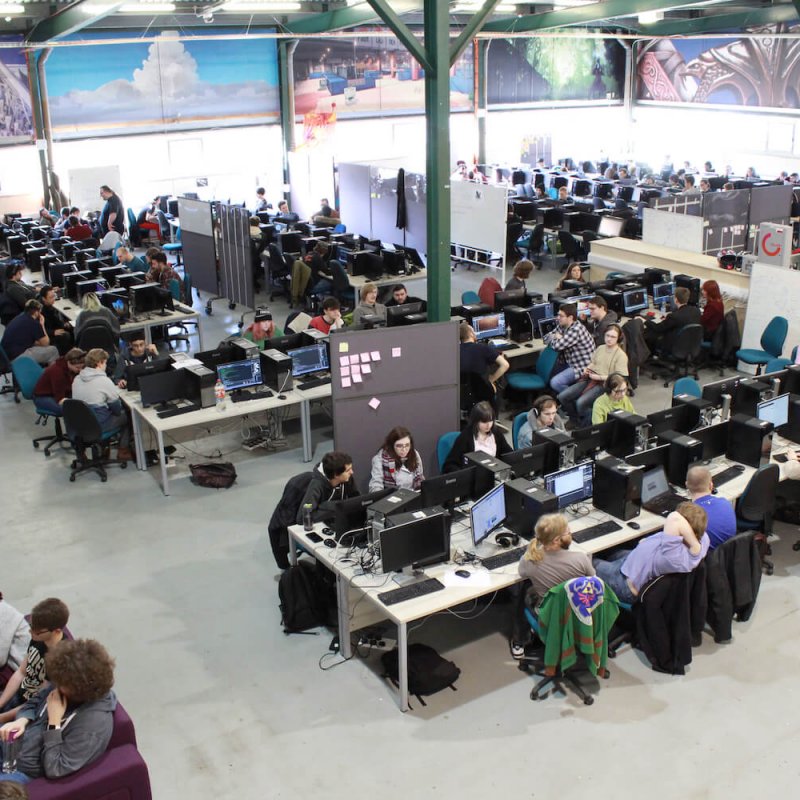 A large warehouse full of gaming students at computers and computer artwork on the walls