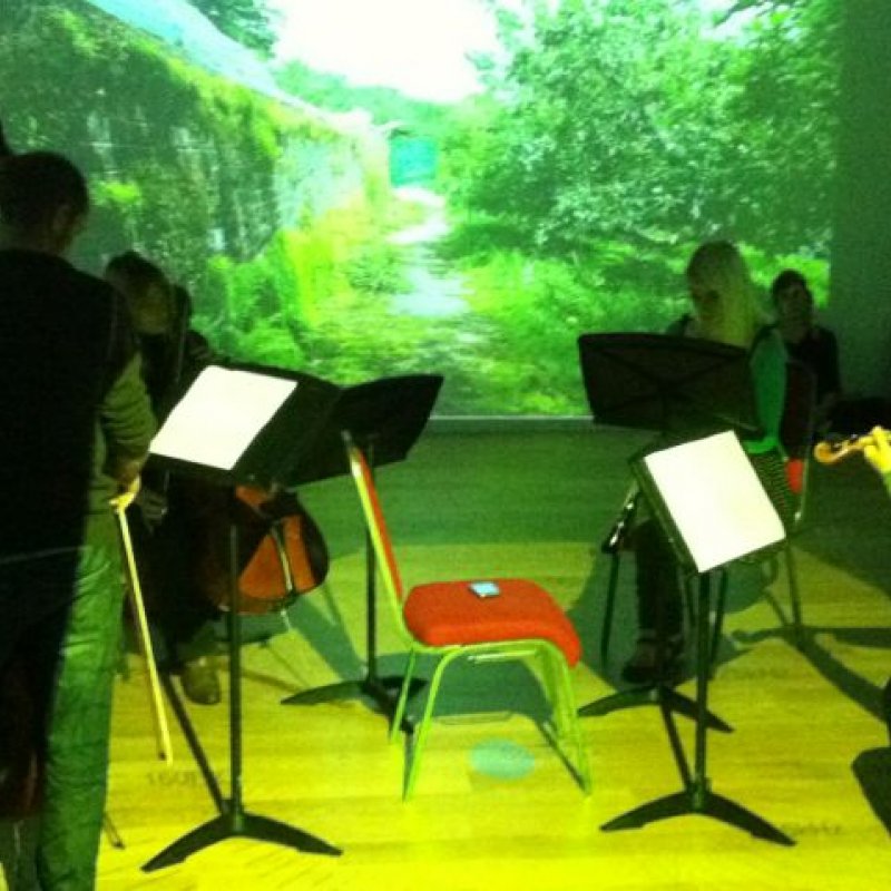 Musicians stood in front of screen with greenery projection