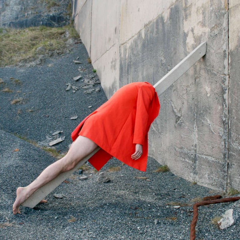 A person in a red coat and bare legs leaning on a pole in an industrial space