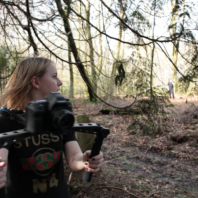 Student in woods with camera on a shoulder mount.