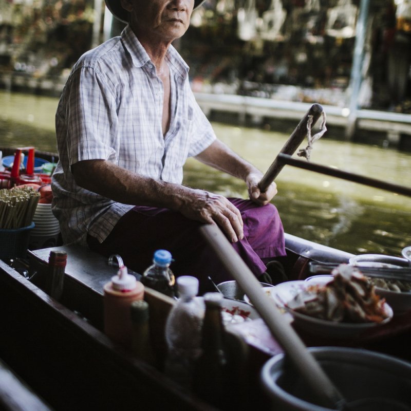 Asian food vendor on boat with food, chopsticks and sauces.