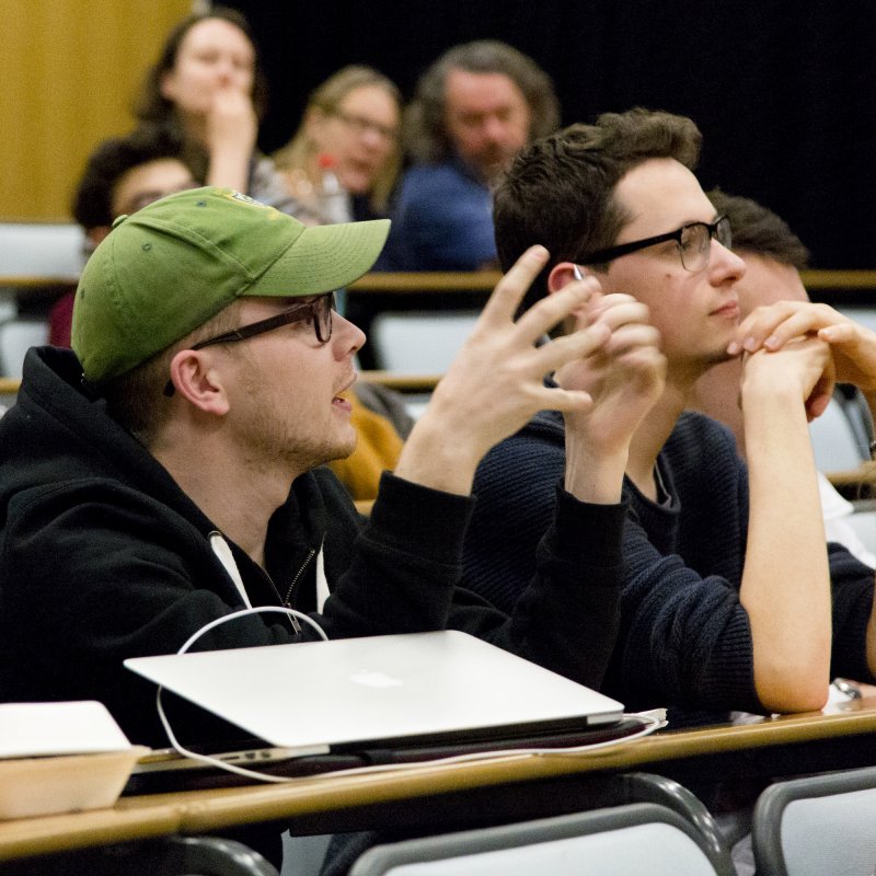 Student wearing green cap engaged discussion in lecture theatre.