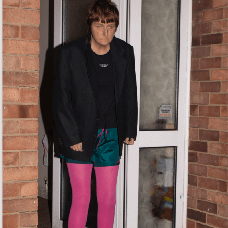 A woman in a doorway, wearing a black jacket and pink tights