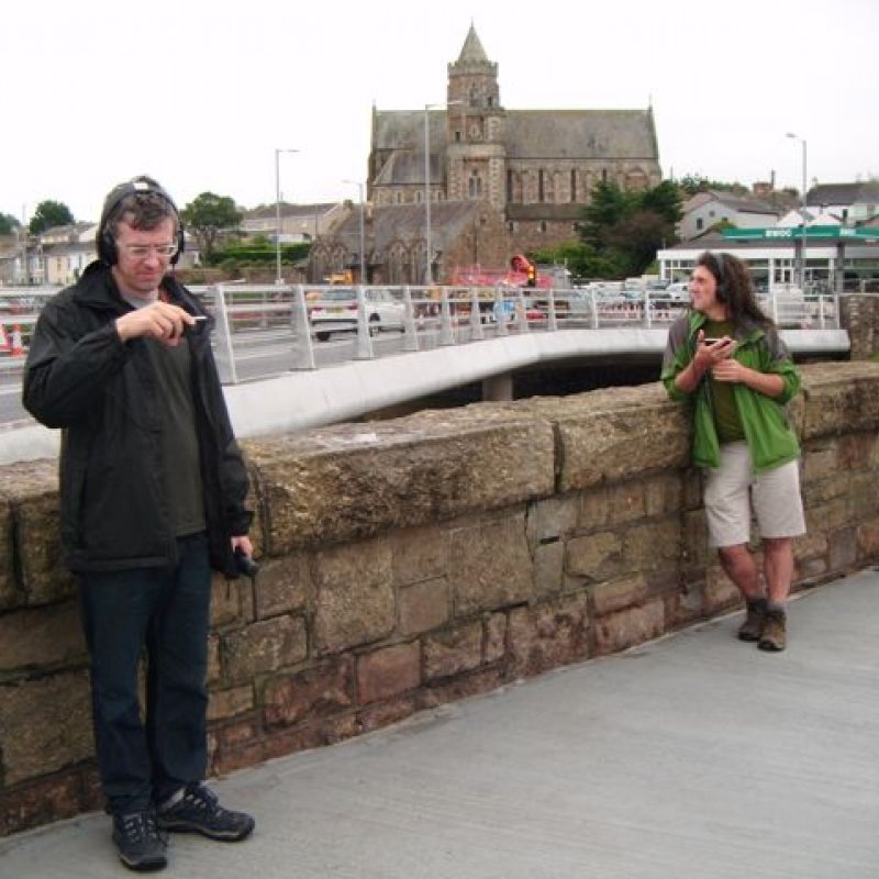 Two men stood on a bridge with earphones