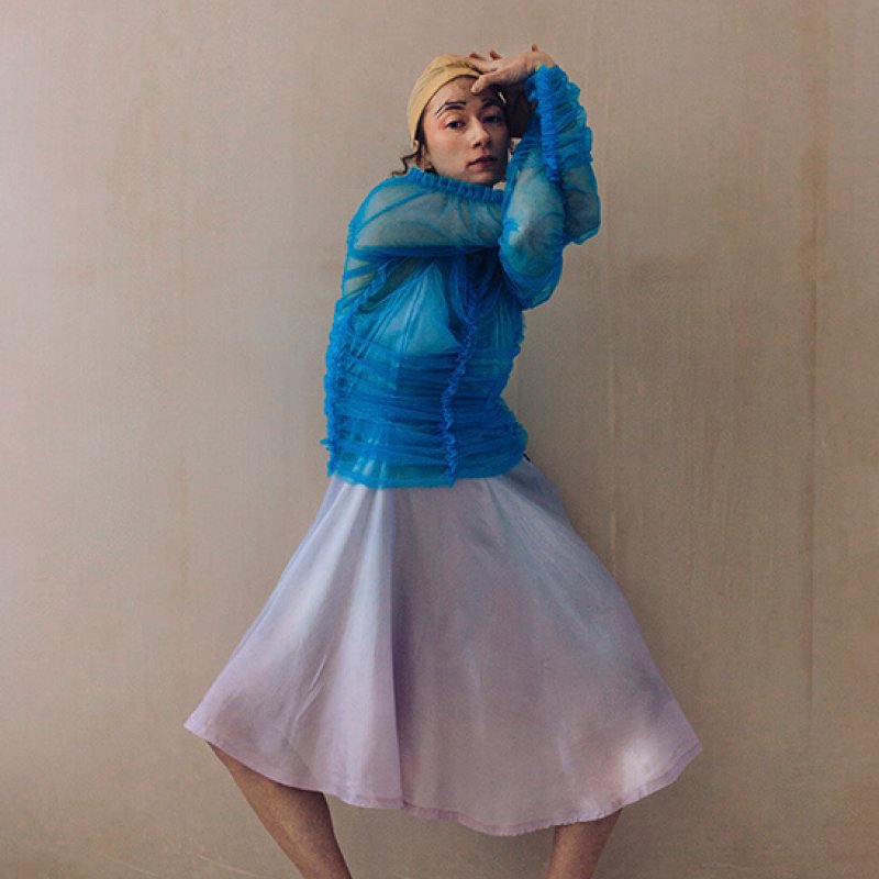 A woman in a blue shirt and pink skirt, wearing clogs