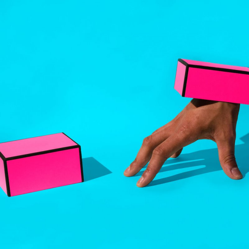 Two pink boxes, one with hand attached and set on a bright blue background.